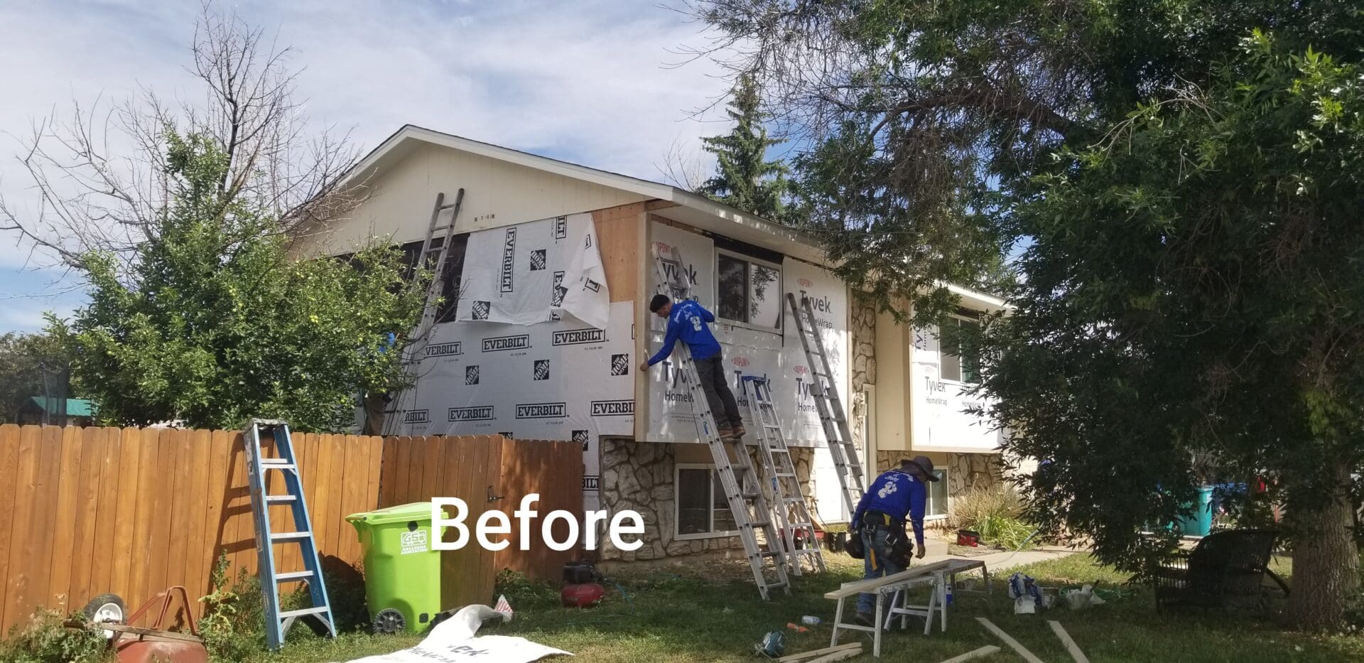 Two workers installing house wrap on the exterior of a house.